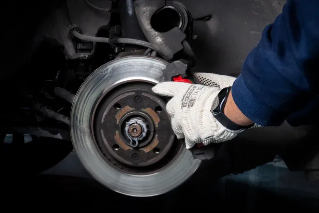 Illustrative photograph of gloved hands servicing a brake disc and caliper