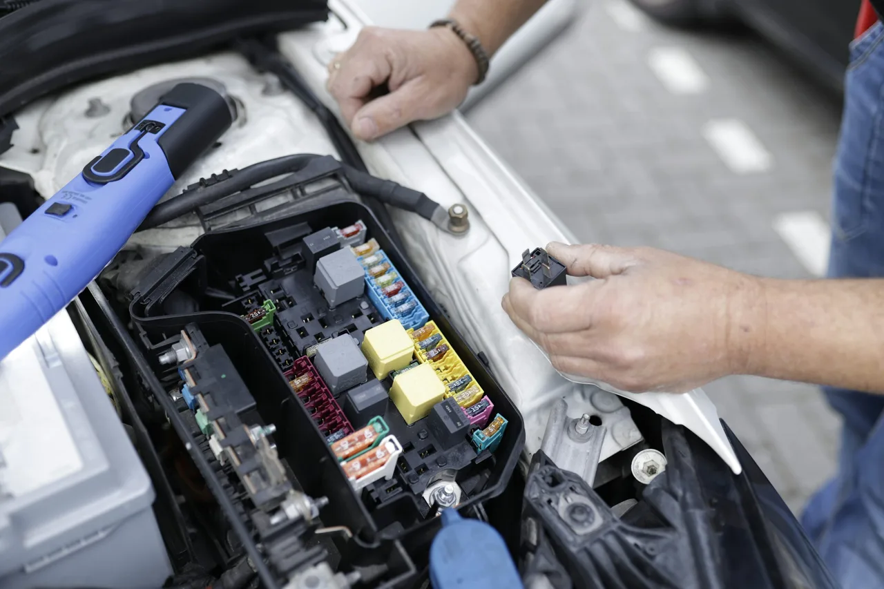 Illustrative photograph of hands inspecting electrical components in an engine bay