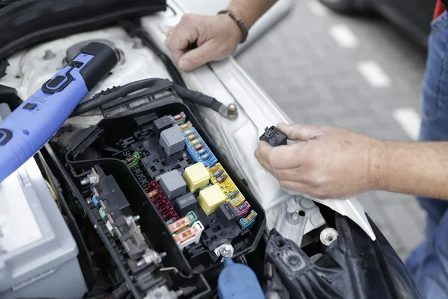 Illustrative photograph of hands inspecting electrical components in an engine bay